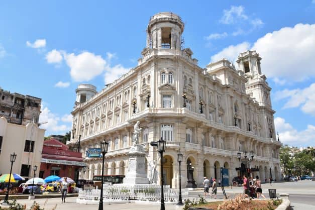 The large white beautiful building that is home to the Museum of Fine Arts in Havana, with archways, balconies, decorative windows, and towers on each of the four corners. 