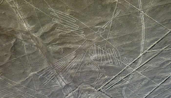 The famous Nazca Lines in Peru seen from the air, depicting something that looks like a bird or an angel with white lines on the greyish green grounds. 