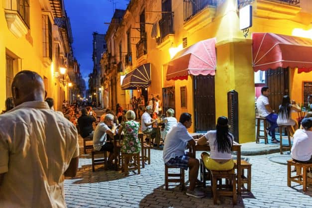 A charming square in Old Havana at night, with outdoor seating conencted to the old city restaurants, with warm lighting and a cozy atmosphere. 