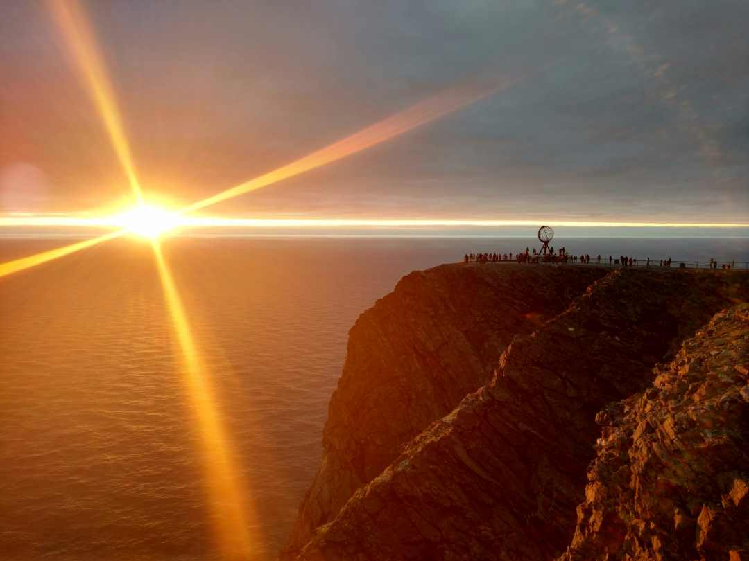 The North Cape on a clear day with a magic golden midnight sun over the horizon above the dark blue sea.