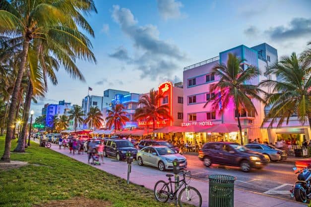 Ocean Drive on South Beach around sunset with neon lighting coming on the buildings amindst palm trees, people and life. 