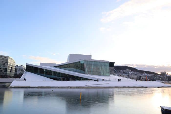 Is Oslo worth visiting? The opera house which is shaped like a glacier in the inner Oslo Fjord, looking like it is sliding into the fjord. The photo is taken on a clear winter day, with blank ice on the water, and pale blue sky. 