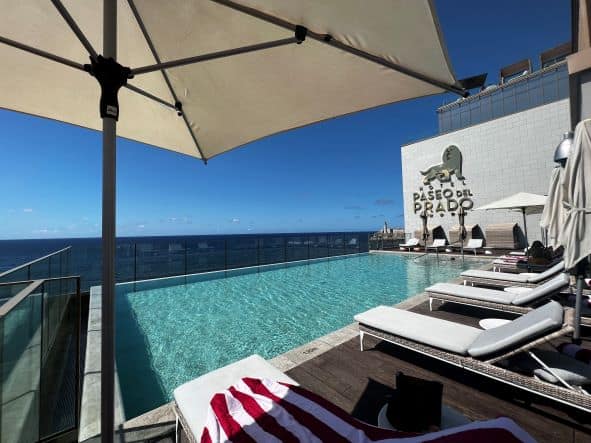 The pool area on a rooftop of the Royalton in Havana (former Padeo del Prado) on a sunny summer day, with delicate sun beds and parasols, and the dark sea and blue skies in direct view. 