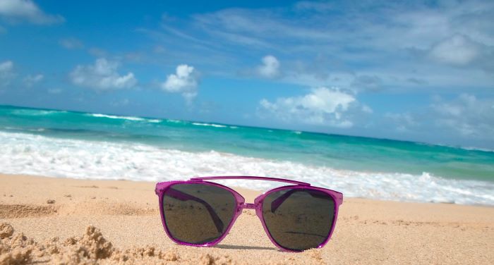 A pair of purple sunglasses on the sand on Playa Grande in the DR, with the crystal clear bluish ocean and sky in the background