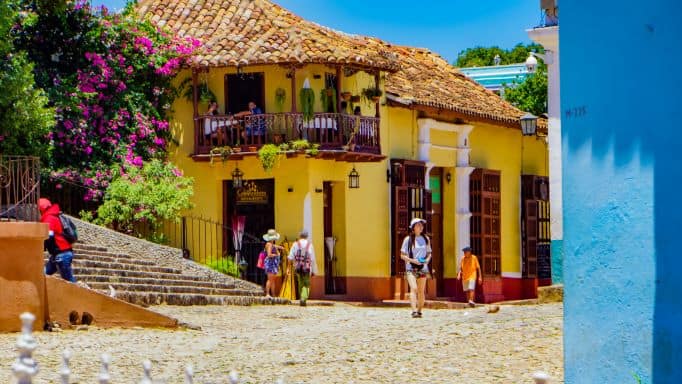 Plaza Mayor and the stone stairs in Trinidad Cuba on a bright sunny day. A local restaurant in a bright yellow stone building with lots of flowers is on the corner of the plaza. 