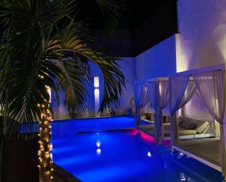 The mansion I rented for my birthday in Miramar, Havana. This is after dark, the backyard pool is lit and bright shiny blue, the sun beds with white curtains behind it is delicately places in the pool, and the palm trees are covered in white small light bulbs. 