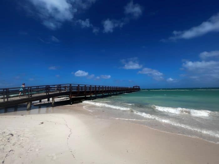 The Punta Cana beach pier stretching from the white sands into the crystal clear ocean on a sunny day with blue skies