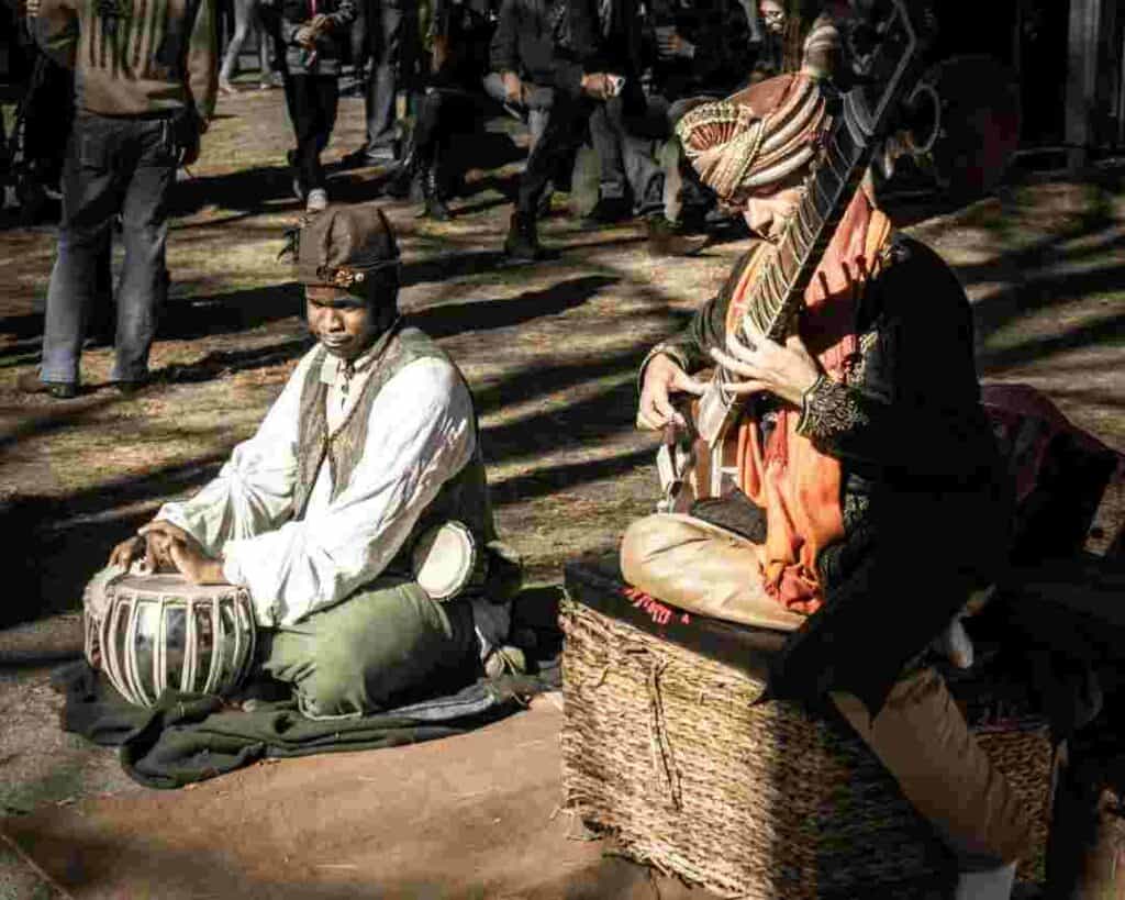 Two trubadeurs seated on the ground playing old fashioned instruments in custumes from the middle ages