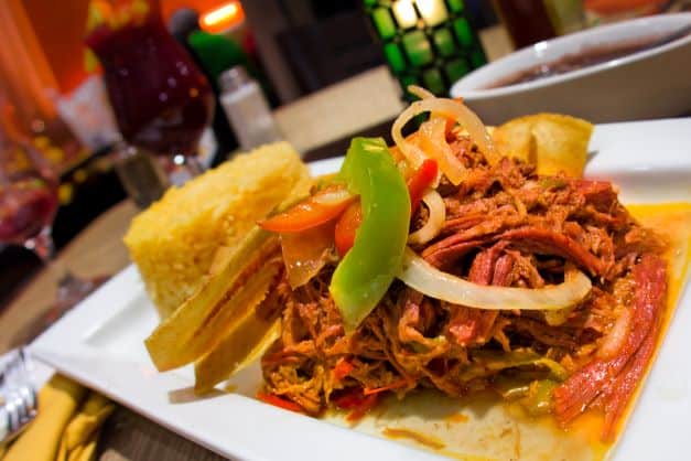 Traditional Cuban ropa vieja served on a white plate decorated with paprika and onion, with rice on the side