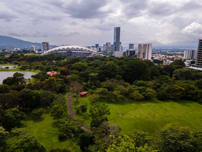 the green fields and forest of Sabana Metropolitan Park in San Jose, with the city scape in the bakcground under a clouded sky