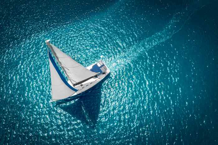 White sailboat with full white sails on dark greenish blue shiny waters seen from above