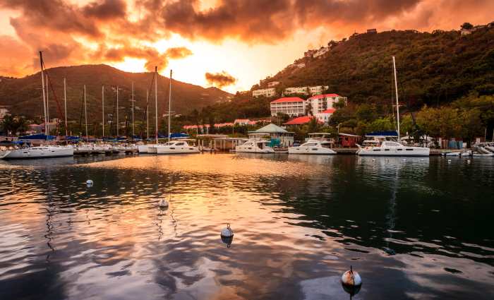 Sunset over Wickhams Kay on Tortola, the sunset reflected glowing in the water, white boats, and the green hills in the background