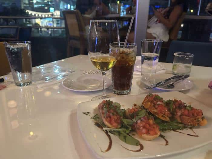 The table from a restaurant I visited, with tomato bruchettas, a glass of wine and a soft drink on a white cloth table at night