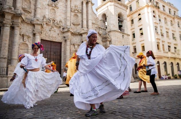 Women in wide white dresses and head wear dancing on a square in Havana