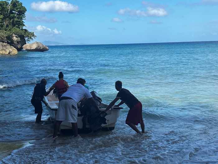 The guys pushing the small dive boat from the beach into the blue ocean from Susoa Beach, on a sunny day. 