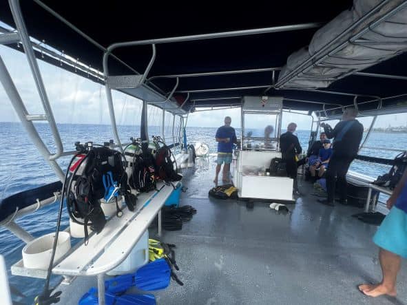 From the scuba diving boat I did a tour with in Grand Cayman, heading out to sea. The boat deck is flat, gray, and divers are prepping for the exit, gear lined up along the railings. 