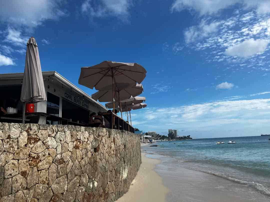 A cozy beach bar along Seven Mile Beach slightly elevated behind a wall, with the water reaching almost all the way up to the stone wall