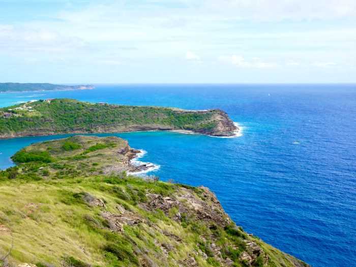 Stunning views from Shirley Heights of green hills steeping down into the deep blue sea, against the pale blue horizon on a sunny day