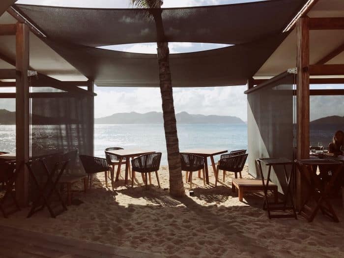 Stunning beach bar view at St Barth with ceilings of fabric and white materials, shaded from the sun, sitting right on the sand with the beach and sea right outside
