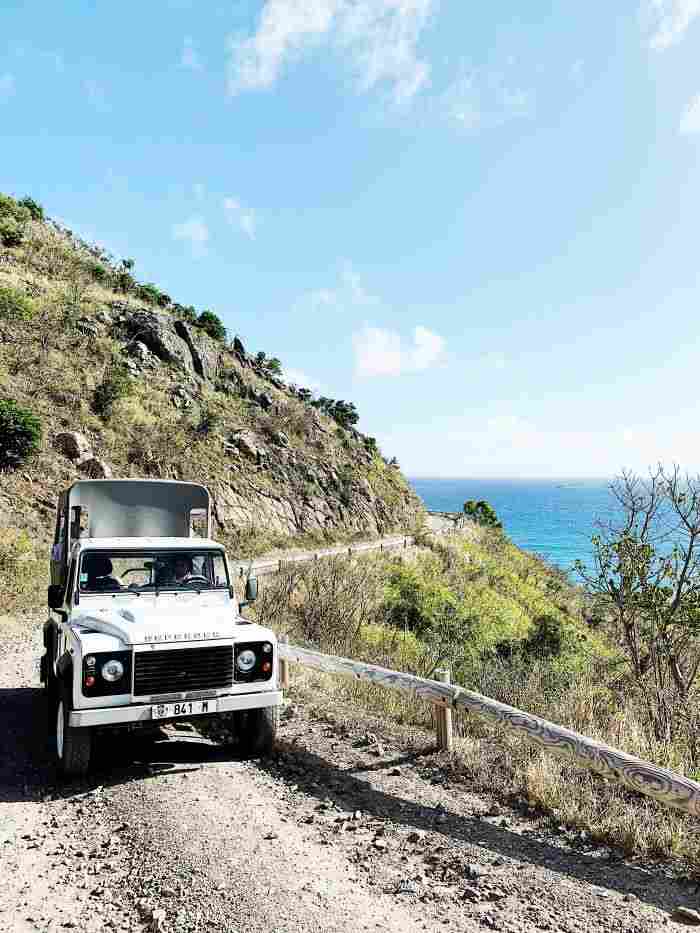 Exploring St Barth on a dirt road in the hills with the blue sea below, in a white jeep range rover