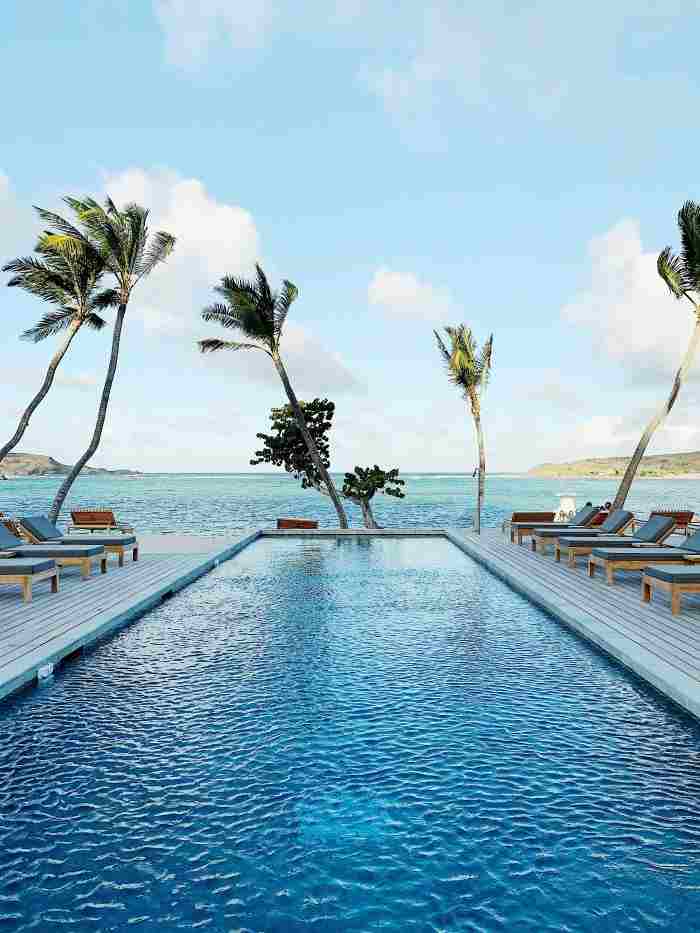 Luxury villas and residences in St Barth, like here with a stunning blue infinity pool with a few palm trees, sun loungers, and infinite views of the sea