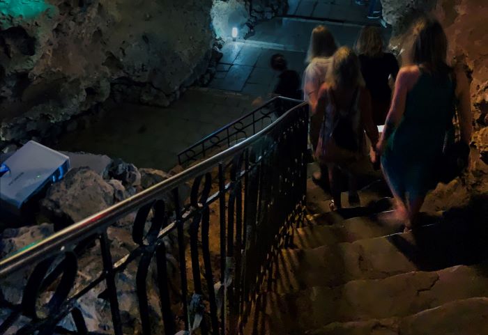 The dimly lit stairway to get down to the club Disco Ayala! Three ladies are walking down in summer dresses, towards the rocky hall beneath. 