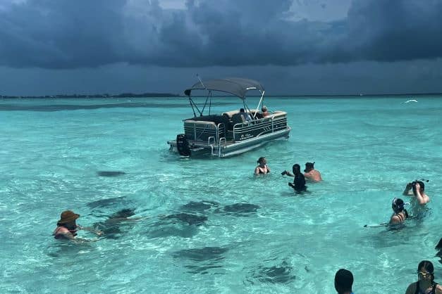 The crystal clear waters at Stingray City in the middle of the ocean, with lots of people in the water and the shadows of the stingrays swimming below the surface.