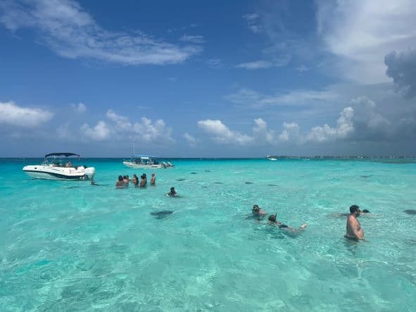 The incredible light blue waters over the sandbank at Stingray City, where people walk with water to their waist, avoiding the stingrays swimming between their feet on a bright sunny summer day. 