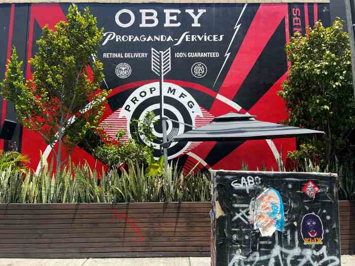A wall mural in Wynwood Miami in bright red and black on a sunny day, surrounded by green trees and bushes