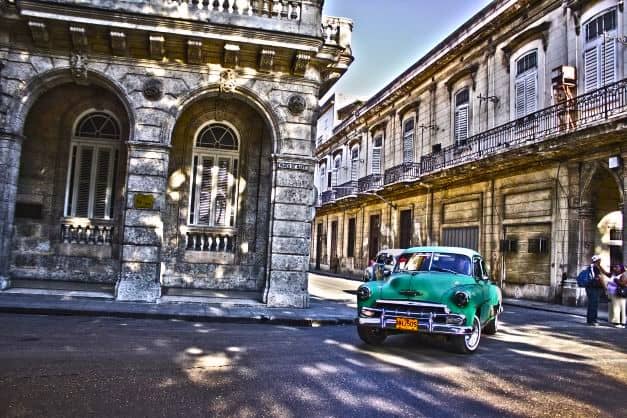 A street corner in Old Havana surrounded by colonial house architecture, and a bright green classic American car turning the corner