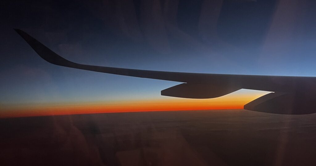 Sunset from the plane window, glowing in the distance with the relieff of a wing in front. 