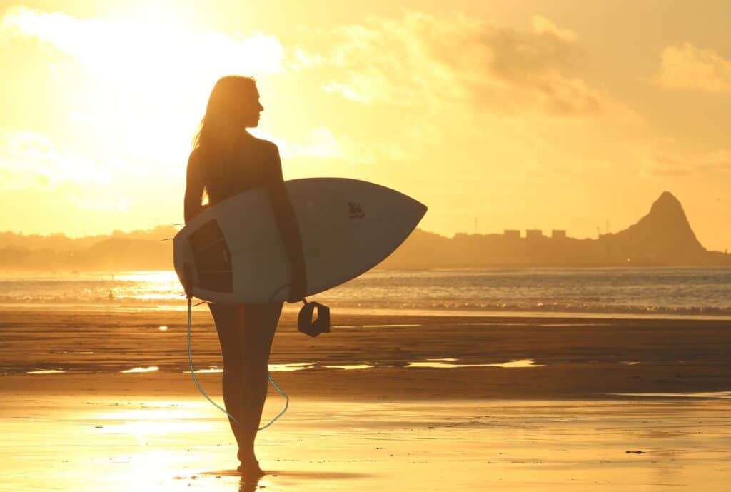 Solo female traveling surfer in sunset on the beach
