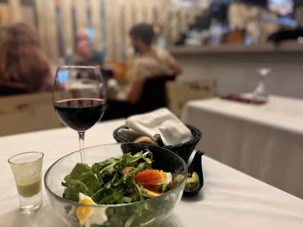 A close up photo of a salad, bread and a glass of red wine on the white table cloth of the 5 Sentidos paladar in Havana at night. 