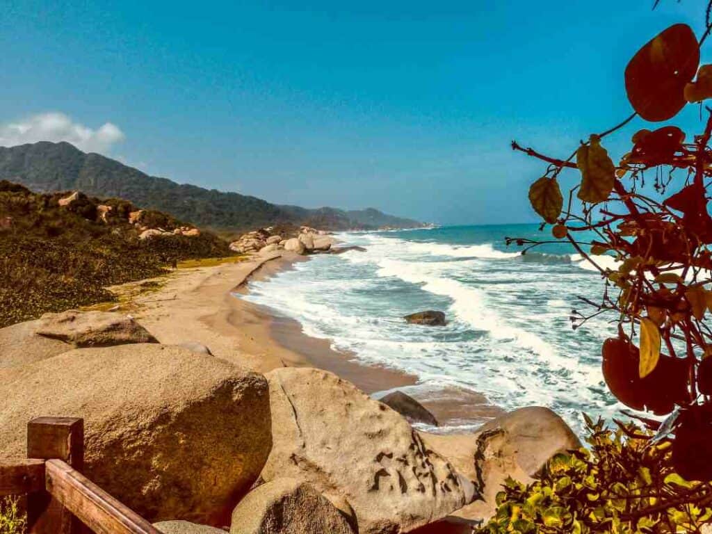 Beautiful golden beach with fierce white waves on Tayrona National Natural Park, with green hills in the background