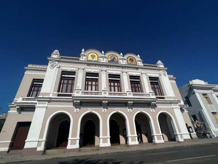 Teatro Tomas Terry in Cienfuegos in a warm beige color with white details, tall archways in the facade towards the street, and a small balcony on the second floor. 