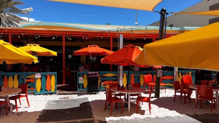 The Rockaway Restaurant on Clearwater Beach Florida, with lots of colored parasols in red, yellow and orange, and outdoor seating in the shade. A bright sunny summer day with blue skies. 