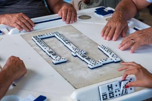 A close up photo of a domino game in little Havana in Domino Park. You see the chips, and all the players hands 