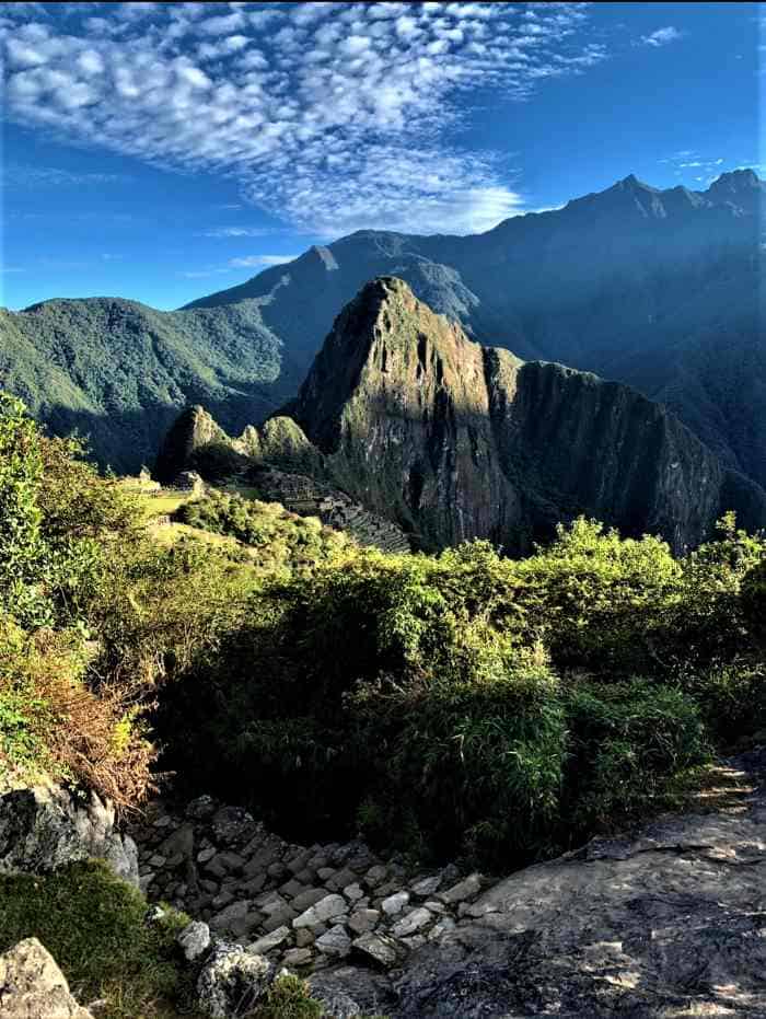 Walking the path surrounded by greenery towards Machu Picchu that can be seen secluded below, surrounded by high mountains
