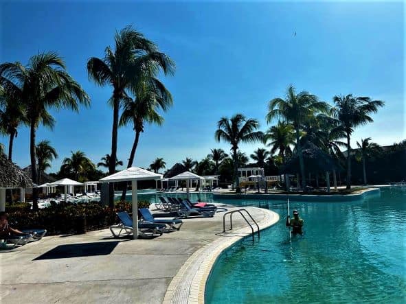 Photo from a beautiful resort in Varadero Cuba, the large resort pools over a big area, surrounded by palm trees, white parasols and blue sun beds. 