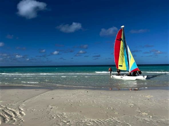 Outside the Royalton Resort in Cayo Santa Maria, where a white catamaran with a red, yellow and blue sail is lying in the calm surf in front of the blue ocean and sky