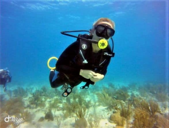 Scuba diving in Cuba on a shallow nature dive with grassy and sandy bottom, with lots of light and sun! I am wearing a black wetsuit and yellow regulator, against the blue ocean behind me. 