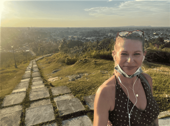 A selfie of me and the view from the top of La Loma hill in Cienfuegos, with the city full of green trees in the background around sunset