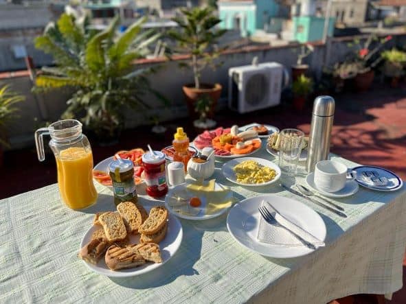 Casa Particular rooftop breakfast table in Cienfuegos, Cuba, with fresh juices, coffee, fruits, cheese, ham, and more on a sunny morning. 