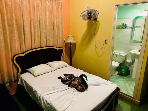 My room at the casa particular in Cienfuegos, Cuba, which is a typical casa you can find around Cuba. The walls are bright yellow and orange, the curtains shiny embroidered, the bathroom is green, and there is an elaborate swan created by colorful towels on the bed. 
