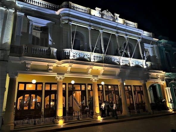 An elegant classic white building at night, where there is a restaurant, bar, and hotel. The facade is decorated with wide columns and ornate details. 