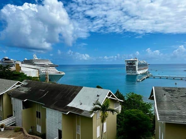 Views from the hills of Ocho Rios towards the cruise harbor, where you see two white elegant cruise ships docked by the jetties on the blue water