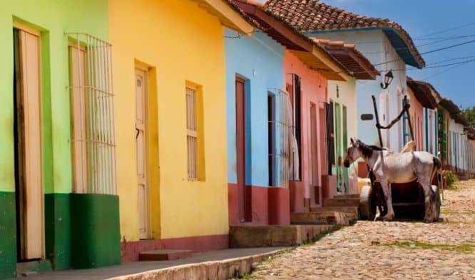 Colorful low houses in Trinidad along a cobblestoned street, with a horse a few houses up. 