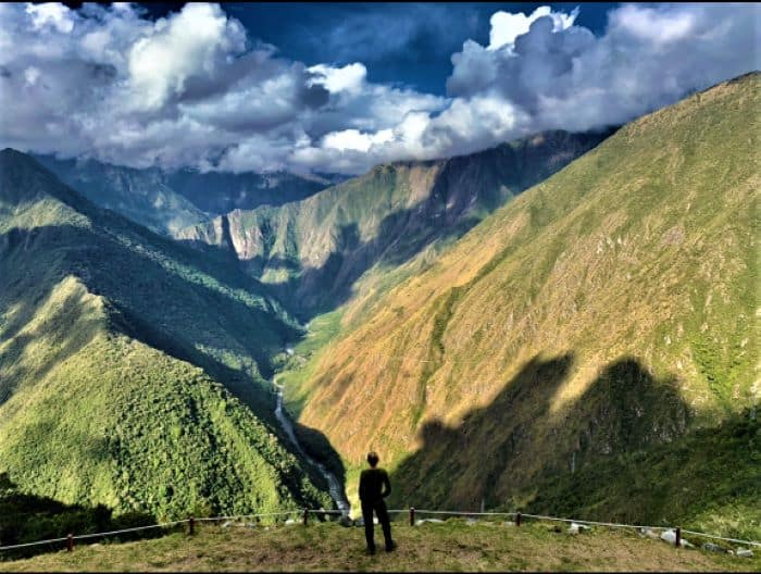 Incredible views along the inca trail; I am standing on a lookout point with infinite views down a green deep valley where you see the mountains ahead stretching forever, under floating clouds in the sky