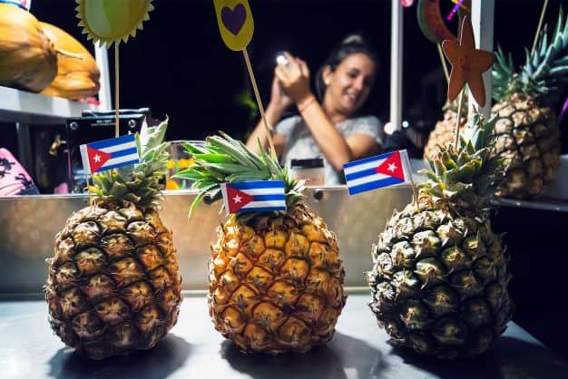 A bartender making pina colada drinks in Varadero at night, in front of the photo are three pineapples with Cuban flags in them. 