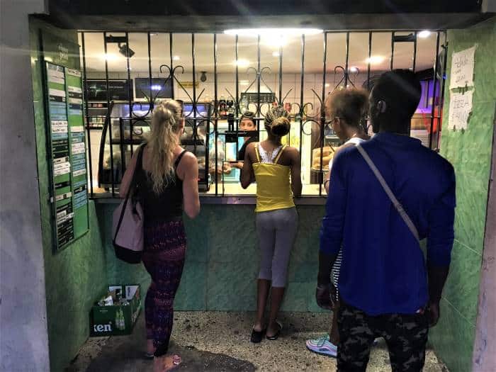 A traditional Ventanita in Havana, where you can get coffee, soft drinks, pizza, sandwiches and whatever is available. This is me standing in line at a Ventanita at night, where the windows are barred with iron rails between the green walls. 